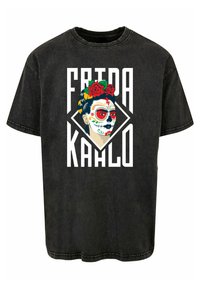 Melna pārproduzēta T-krekla ar krāsainu Frida Kahlo grafiku, rotāta ar ziedu akcentiem un dekoratīvām galvaskausa make-up. Bold teksts zem attēla.