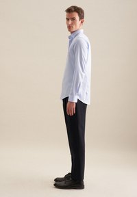 Jasnoniebieska koszula z długim rękawem i spiczastym kołnierzykiem, zestawiona z ciemnymi spodniami i czarnymi butami. Gładka tkanina, dopasowany krój.