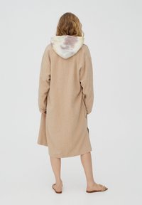 Vestido largo de lino beige con capucha de patrón tie-dye en la parte trasera. Presenta un ajuste holgado y mangas largas. Diseño simple y sin adornos.