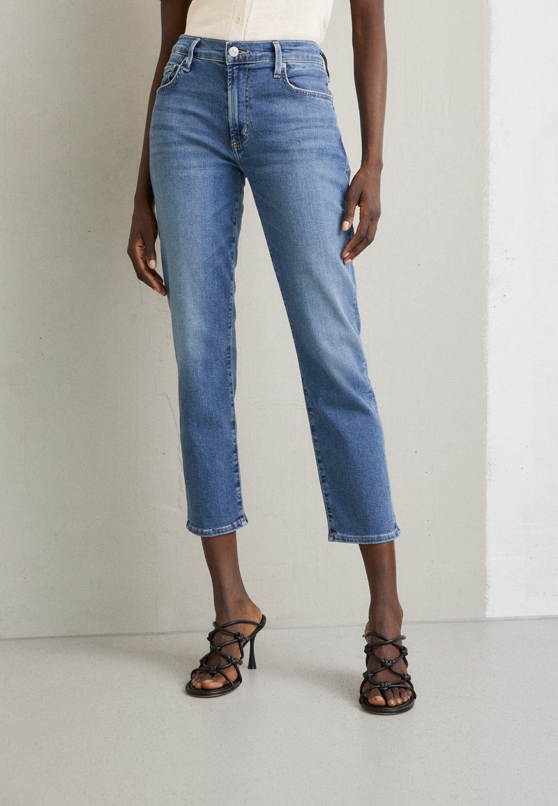 Světlomodré cropped džíny s rovnými nohavicemi a třepeným lemem, spárované s černými sandály na vysokém podpatku se strapci. Texturovaná látka a klasický design.