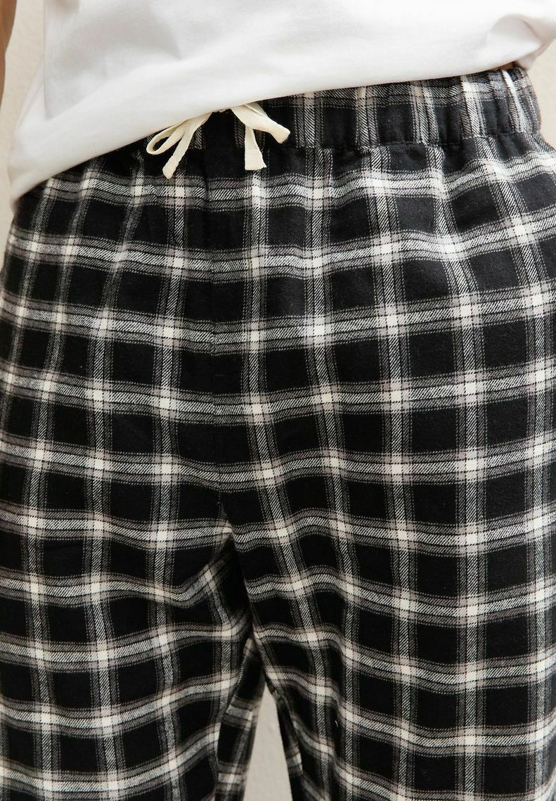 Un pantalon de pyjama à carreaux en noir et blanc avec une taille élastique munie d'un cordon de serrage et un tissu doux et texturé.