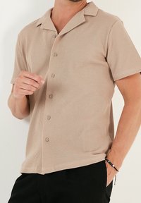 Kortärmad, beige knapp-up skjorta med en texturerad väv och rak krage. Har fem knappar framtill och en avslappnad passform.