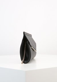 Clutch nera in finta pelle con tracolla in oro, chiusura a patta piatta e superficie texturizzata. Ha la forma di un piccolo sacchetto.
