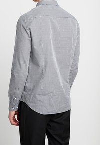 Chemise à manches longues, ajustée, en tissu lisse, à carreaux noir et blanc, avec col et ourlet arrondi.