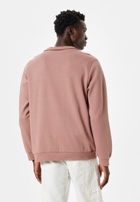 Bordowy sweatshirt o luźnym kroju, z prążkowanymi mankietami i dolnym wykończeniem. Miękka tekstura i minimalistyczny design, z małym kołnierzykiem przy dekolcie.