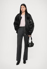Schwarze Bomberjacke mit einem runden Aufnäher, hellrosa Oberteil, graue taillierte Hose und eine kleine schwarze Handtasche mit Nieten. Schwarze Peep-Toe-Stiefel.