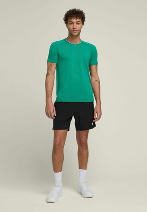 Groene sportshirt met korte mouwen en een ronde halslijn, gecombineerd met zwarte shorts en witte sneakers. Glad materiaal en aansluitende stijl.