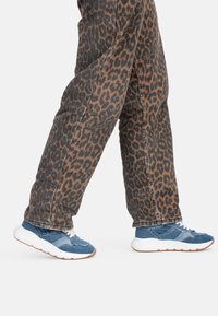 Jeans in denim con stampa leopardata abbinati a sneakers sportive blu e bianche con una parte superiore testurizzata e una suola bianca spessa.