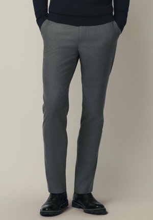 Szare spodnie w slim fit o gładkiej fakturze, z płaskim przodem i bocznymi kieszeniami, zestawione z czarnymi skórzanymi butami.