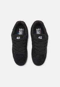 Black sneakers featuring suede material, round toe, and flat laces. Accented by logos inside, textured surface, and contrasting blue detail.