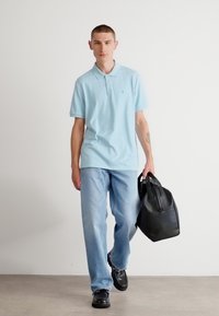 Lyseblå polo t-shirt med korte ærmer, parret med lyse vaskede jeans. Sort lædertaske i hånden, mørke sko fuldender looket.