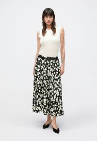 Biele tielko bez rukávov v kombinácii s čiernou midi sukňou s kvetinovým vzorom v bielej a zelenej farbe. Čierny opasok v páse a čierne topánky.