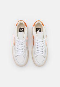 Baskets blanches avec des accents en daim orange, bout rond, fermeture lacée et semelle en caoutchouc beige. Tige en cuir lisse avec une finition texturée.