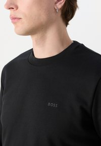 Melns crew neck džemperis, kas izgatavots no mīksta kokvilnas, ar smalku logotipu atbilstošā krāsā uz krūtīm. Gluda tekstūra un pielāgota forma.