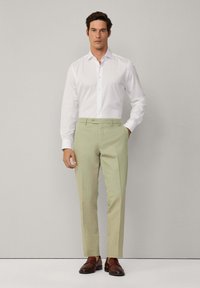 Weißes Hemd mit langen Ärmeln, hellgrüne Hose und braune Schuhe. Glattes Material, taillierte Passform und klassischer Schnitt.