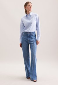 Camicia button-up a righe blu chiaro e bianche con maniche lunghe, abbinata a jeans blu a vita alta e svasati, e sandali neri con tacco.