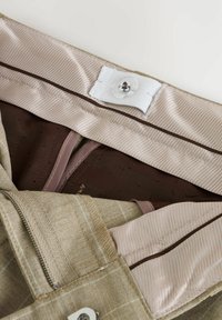 Tessuto a quadri beige con una fodera interna liscia e lucida; presenta una chiusura con bottone e un dettaglio di tasca con zip.