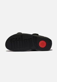 Zwarte zool met reliëf "fitflop" logo, gestructureerd oppervlak en rode cirkelvormige detail. Het bovendeel heeft banden van een donkere, glinsterende stof.