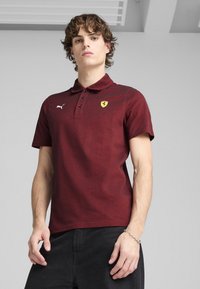 Burgundská polo košeľa s textúrovaným povrchom, s trojbuttonovou légou, logom Puma a žltým erbom Ferrari na ľavej hrudi.