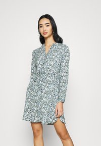 Abito a maniche lunghe con un motivo floreale in blu e verde. Presenta una scollatura a V e una vita arricciata che si allarga verso l'orlo.