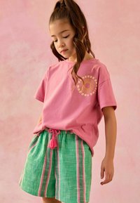 T-shirt en coton rose avec un graphique de soleil, associé à un short rayé vert et rose dotée d'une ceinture à cordon avec un accent de pompon.