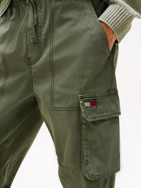 Olivgrön cargo-byxor gjorda av mjukt tyg, med sidofickor och en lapp med "TOMMY JEANS"-logotyp. Resårmidja med dragsko.
