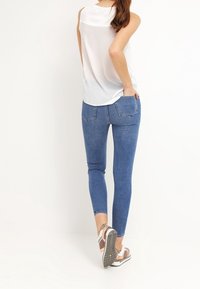 Jeans skinny in denim blu con una texture liscia e un minimo scolorimento, abbinati a un top senza maniche bianco e scarpe casual.