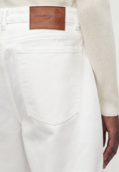 Λευκά τζιν από τζιν με πίσω τσέπη και καφέ δερμάτινο λογότυπο με την επιγραφή «Officine Générale Paris 6», φορεμένα με κρεμ ριμπ πουλόβερ.