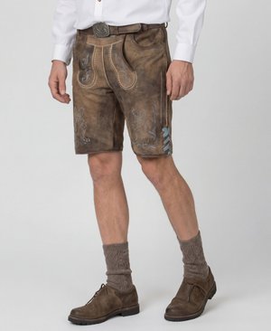 Mann trägt traditionelle braune Lederhosen mit dekorativer Stickerei, beigefarbene Wollsocken, braune Schuhe und ein weißes Hemd.