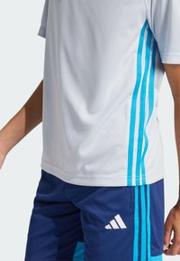 Camiseta deportiva blanca con acentos azules y tres rayas en las mangas, combinada con pantalones cortos azul marino que tienen un logo blanco y paneles laterales azules.