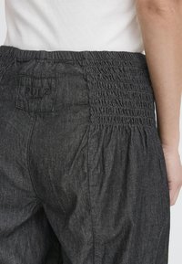 Pantalons en denim noir avec une taille froncée. Présente une petite étiquette à l'arrière avec "PULZ" et une finition douce et texturée.