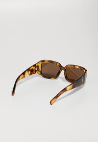 Tortoiseshell sunglasses with brown lenses, angular design, smooth plastic frame, and slender arms featuring a subtle logo detail.