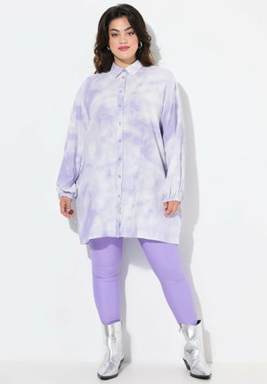 Hellblau-getönte Batik-Hemdkleid mit Kragen, durchgehender Knopfleiste und langen Ärmeln, kombiniert mit lavendelblauen Leggings und silbernen Stiefeletten.