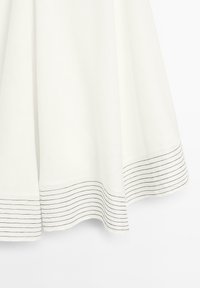 Witte stof met een zoom die zwarte horizontale strepen heeft. De stof lijkt glad en valt elegant.