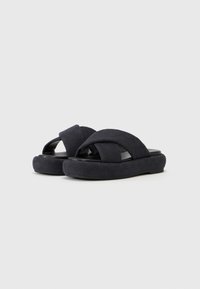 Sorte slip-on sandaler med kryss-sømmede stoffstropper, en teksturert overdel og en tykk, polstret såle for komfort.