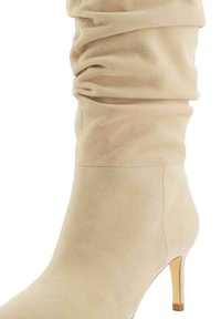 Beige suede ankle boot with a slouchy upper and a thin stiletto heel, featuring smooth texture and seamless construction.