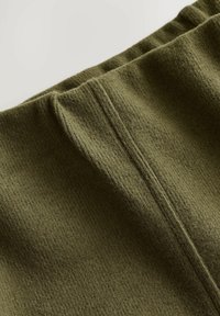 Tissu vert olive avec une texture côtelée et des coutures visibles, présentant un design de taille froncée.