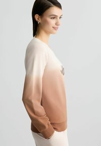 Ombre sweatshirt met een verloop van licht beige naar bruin, zachte stof, lange mouwen en ribgebreide manchetten. Voorzien van decoratieve tekst aan de voorkant.