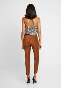 Top con stampa a serpente bianco e nero con orlo arricciato, abbinato a pantaloni aderenti in materiale scamosciato marrone. Vengono indossate scarpe con tacco alto nere a strappo.