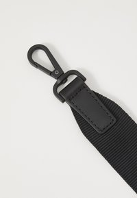 Black nylon strap features a leather accent with stitching, and a black metal clip for secure attachment. Textured surface and sleek design.