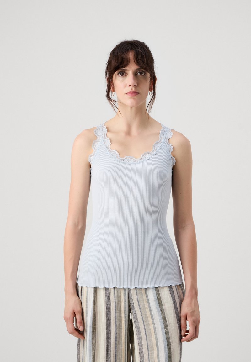 Lys blå ribbestrikket tanktop med bølgende blondekant ved halsen og armhulene, paret med stripete linbukser.