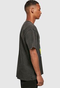Camiseta oversized de algodón negra con mangas cortas, bordes deshilachados y diseño gráfico con elementos coloridos en la parte delantera.