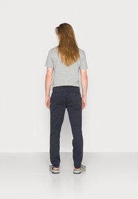 T-shirt gris à manches courtes associé à un pantalon bleu marine, avec une coupe ajustée et deux poches arrière. Des chaussures décontractées complètent le look.