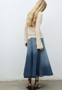 Denim maxi rok met een uitlopende vorm, lichtblauwe wassing en achterzakken. Gekleed met een textuur crème lange mouwen top en bruine hakken.