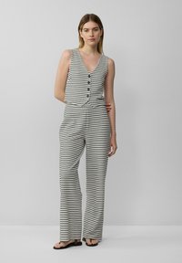 Zwart-wit gestreepte mouwloze top met een v-hals, voorzien van knopen aan de voorkant; gecombineerd met een brede broek in dezelfde stof.