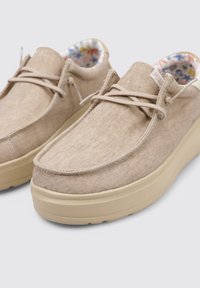 Zapatos de lona beige con punta redondeada y superficie texturizada, que presentan una suela de plataforma de color claro y un forro interior con un patrón floral.