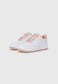 Weiße Ledersneaker mit pinken Akzenten, runde Zehenpartie, perforierte Details, flache Schnürsenkel und Gummisohle. Nike-Logo an der Seite und auf der Zunge.