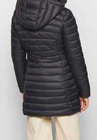 Schwarze Steppjacke mit Kapuze, gestepptem Design und horizontalen Streifen sowie elastischen Bündchen. Glatte Stoffoberfläche mit tailliertem Schnitt.