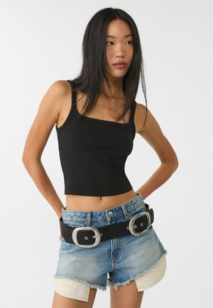 Svart kortad tanktopp med fyrkantig halsringning, i kombination med slitna denimshorts och ett brett svart bälte med silverspännen.