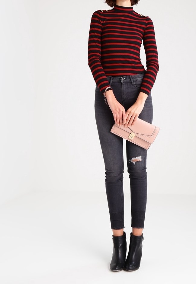 Röd och svart randig långärmad topp, mörka rivna skinny jeans, svarta ankelboots, håller en ljusrosa clutch med nitar.